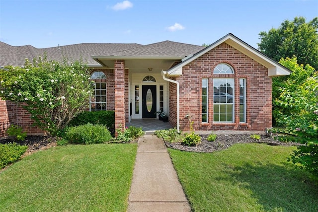 ranch-style house with a shingled roof, a front yard, and brick siding