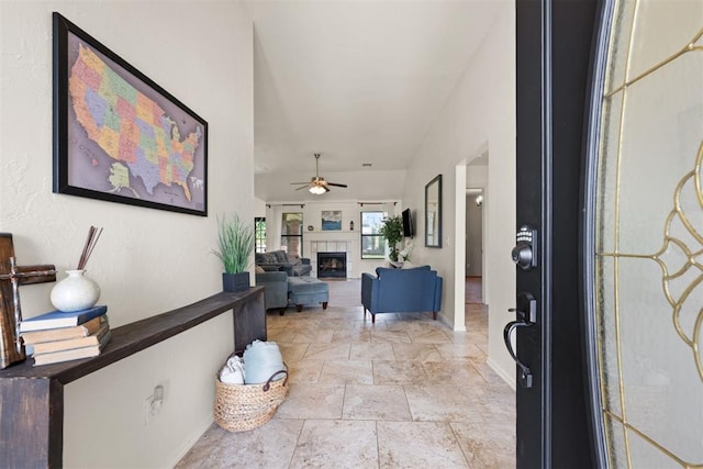 foyer with stone tile flooring, baseboards, ceiling fan, and a tiled fireplace