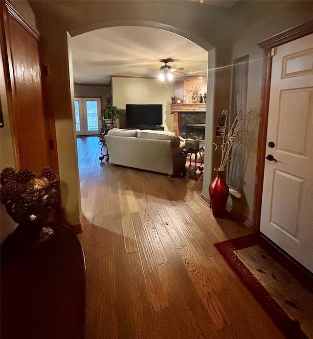 living area with arched walkways, wood-type flooring, ceiling fan, and a fireplace