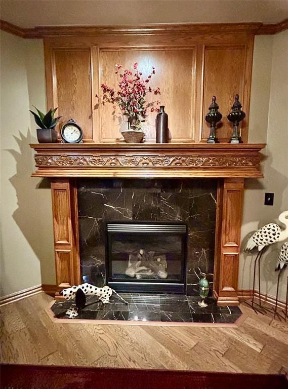 interior details with ornamental molding, a tile fireplace, baseboards, and wood finished floors