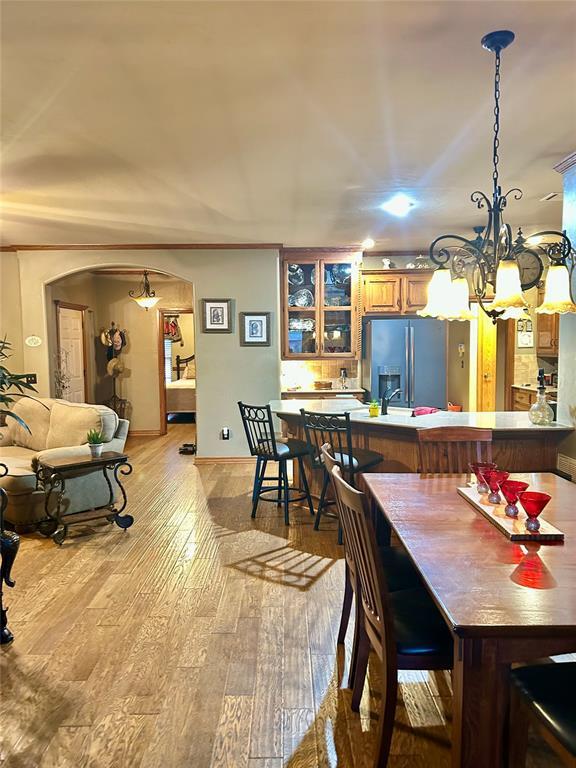 dining area with arched walkways, a notable chandelier, and light wood-style floors