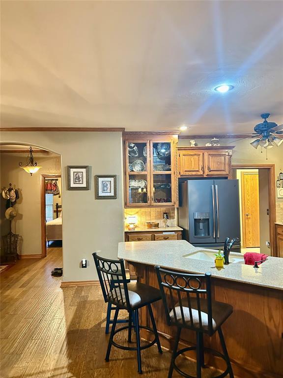 kitchen with dark wood-style flooring, ceiling fan, glass insert cabinets, a kitchen breakfast bar, and refrigerator with ice dispenser