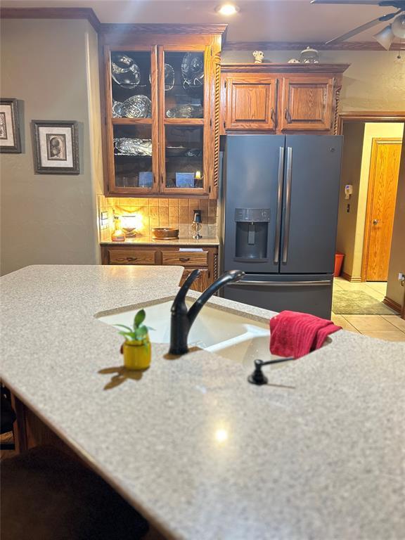 kitchen featuring fridge with ice dispenser, brown cabinetry, light tile patterned floors, glass insert cabinets, and ceiling fan