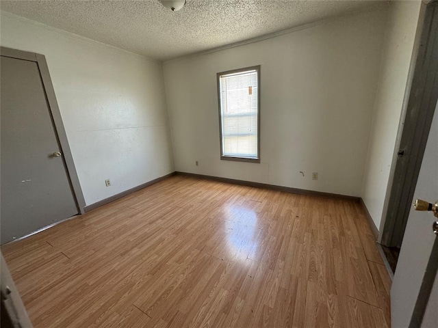 empty room featuring a textured ceiling, light wood-type flooring, and baseboards