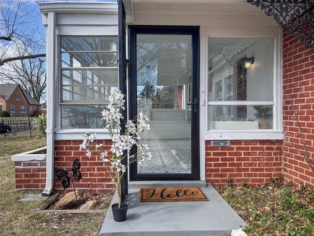 view of exterior entry with fence and brick siding