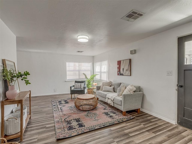 living room with visible vents, a textured ceiling, baseboards, and wood finished floors