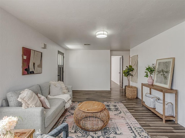 living area with a textured ceiling, wood finished floors, visible vents, and baseboards