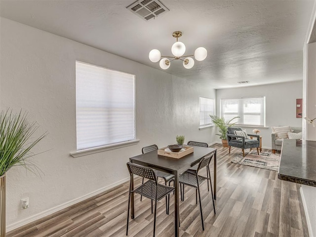 dining area with a textured wall, wood finished floors, visible vents, baseboards, and an inviting chandelier