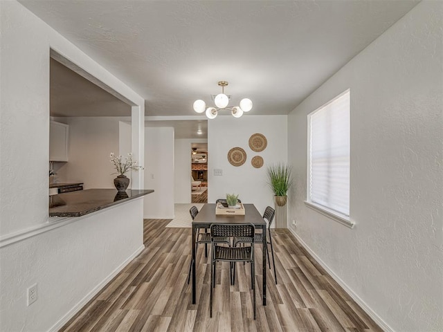 dining room featuring baseboards, a textured wall, wood finished floors, and an inviting chandelier