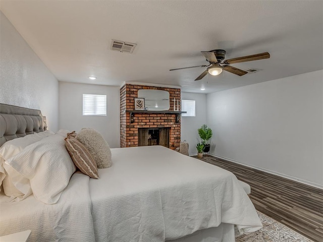 bedroom with a ceiling fan, visible vents, a fireplace, and wood finished floors