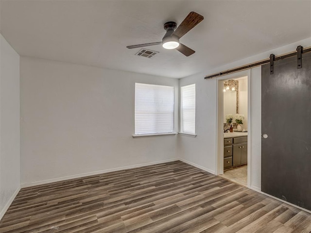 spare room featuring visible vents, a barn door, ceiling fan, wood finished floors, and baseboards