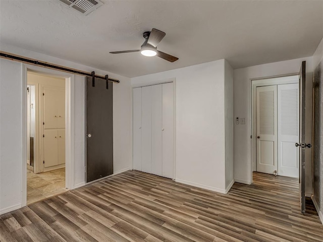 unfurnished bedroom with baseboards, a barn door, visible vents, and wood finished floors