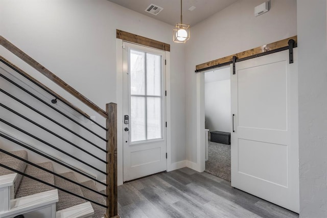 foyer entrance with visible vents, stairs, a barn door, wood finished floors, and plenty of natural light