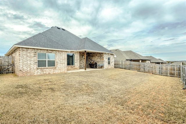 rear view of property featuring a patio, roof with shingles, a fenced backyard, a lawn, and brick siding