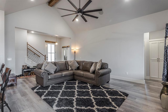 living room featuring baseboards, stairway, beam ceiling, wood finished floors, and high vaulted ceiling