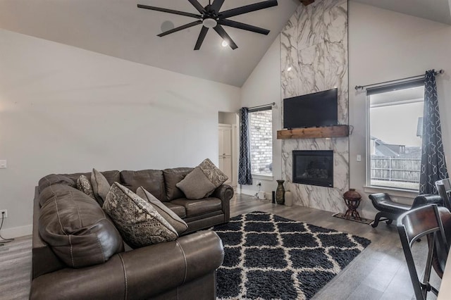 living area with baseboards, a fireplace, wood finished floors, high vaulted ceiling, and a ceiling fan