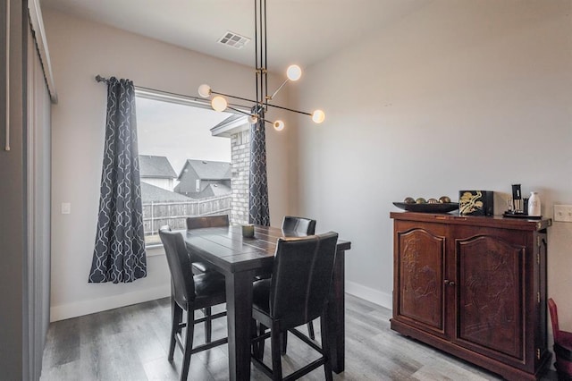 dining space with light wood finished floors, visible vents, a chandelier, and baseboards