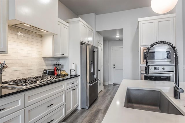 kitchen featuring a sink, wood finished floors, white cabinetry, appliances with stainless steel finishes, and decorative backsplash