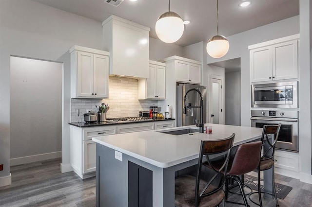 kitchen with stainless steel appliances, wood finished floors, an island with sink, and decorative backsplash