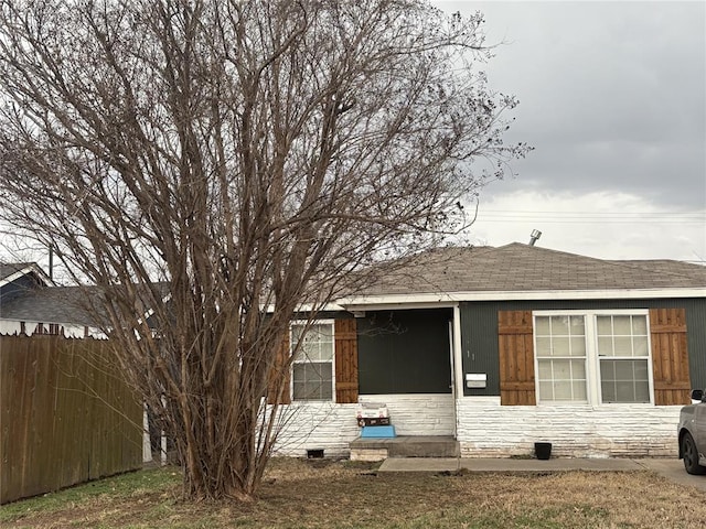 back of property with entry steps, stone siding, a shingled roof, and fence