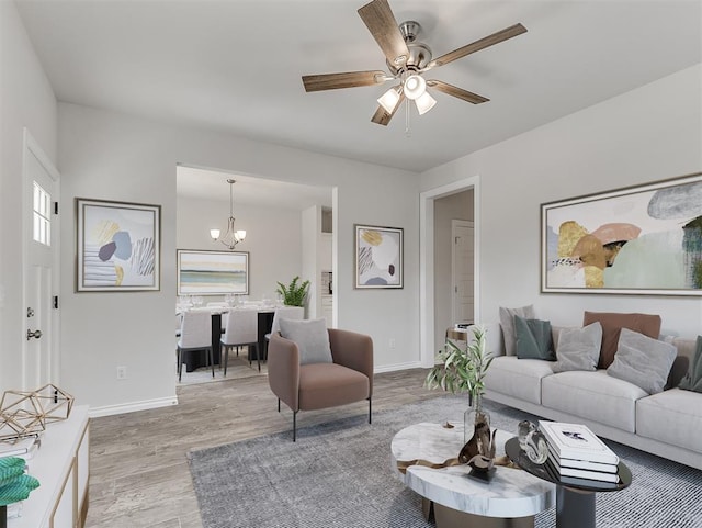 living room featuring light wood-type flooring, baseboards, and ceiling fan with notable chandelier