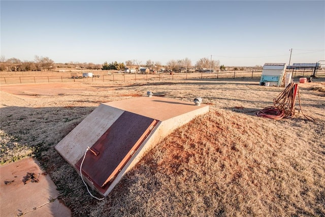 entry to storm shelter featuring fence and a rural view