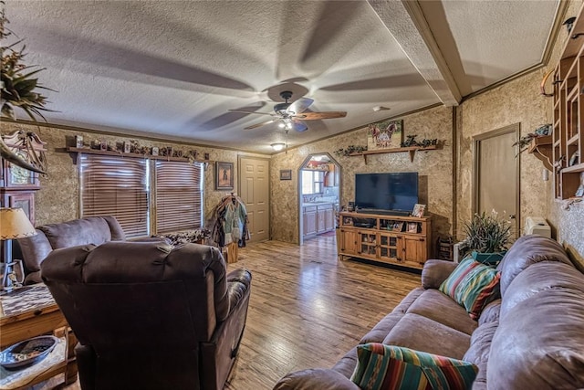 living room with wallpapered walls, a ceiling fan, wood finished floors, vaulted ceiling with beams, and a textured ceiling