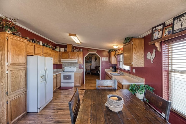 kitchen featuring arched walkways, under cabinet range hood, white appliances, wood finished floors, and ornamental molding