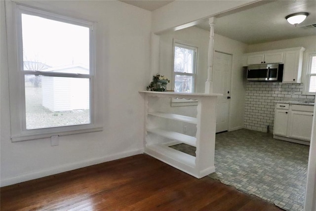 kitchen with baseboards, visible vents, white cabinets, stainless steel microwave, and dark wood-style flooring