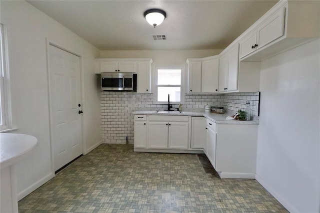 kitchen with a sink, visible vents, white cabinetry, tasteful backsplash, and stainless steel microwave