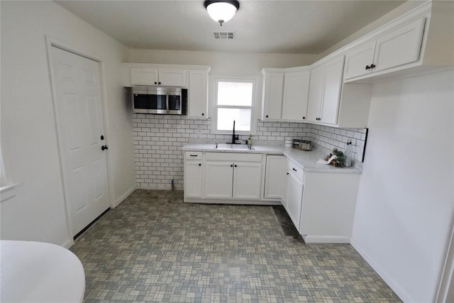 kitchen with stainless steel microwave, visible vents, backsplash, white cabinets, and a sink