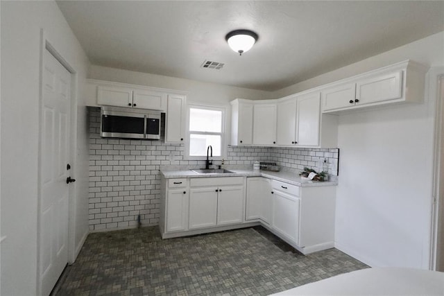 kitchen featuring visible vents, stainless steel microwave, light countertops, white cabinetry, and a sink