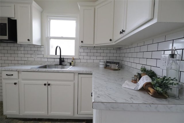 kitchen with tasteful backsplash, stainless steel microwave, a sink, and white cabinets