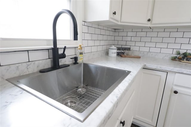 interior details featuring white cabinets, a sink, backsplash, and light stone countertops