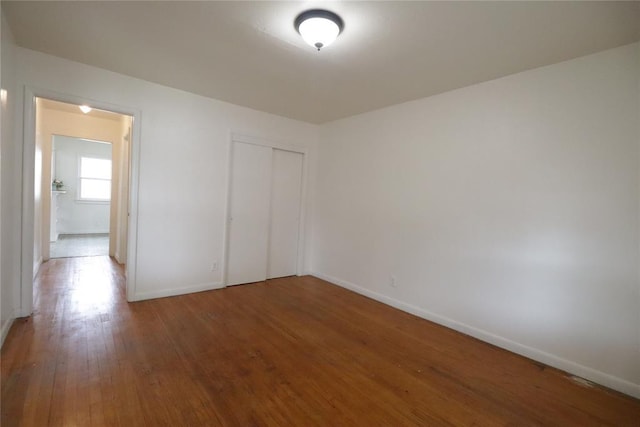 unfurnished bedroom with a closet, baseboards, and hardwood / wood-style flooring