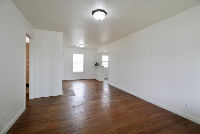 spare room featuring baseboards and dark wood-type flooring