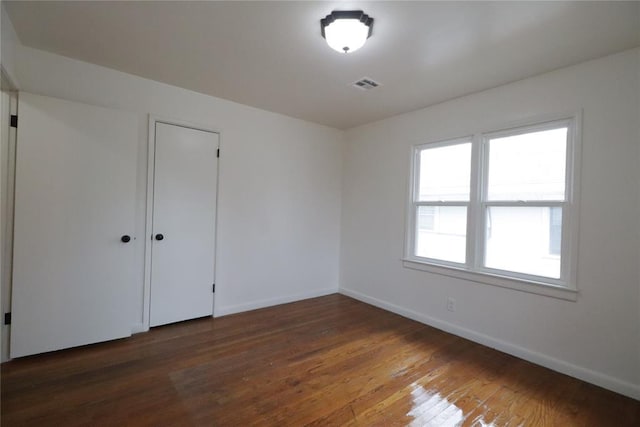 spare room with wood finished floors, visible vents, and baseboards