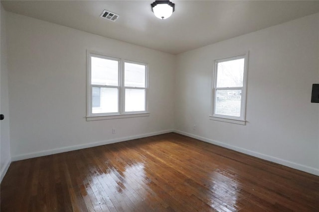 empty room featuring hardwood / wood-style flooring, visible vents, and baseboards