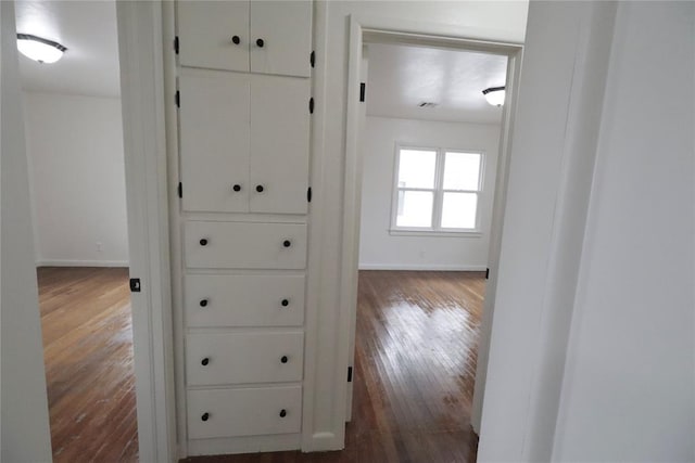 hallway with baseboards, visible vents, and dark wood-type flooring