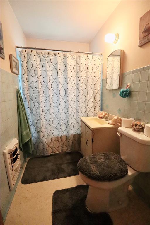 bathroom with curtained shower, a wainscoted wall, tile walls, and toilet