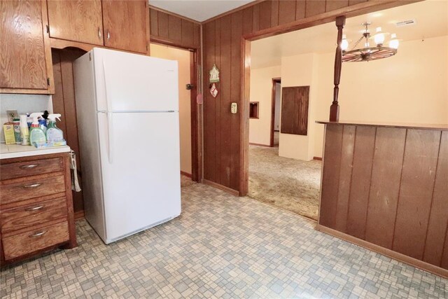 kitchen featuring light countertops, brown cabinetry, freestanding refrigerator, wooden walls, and a chandelier