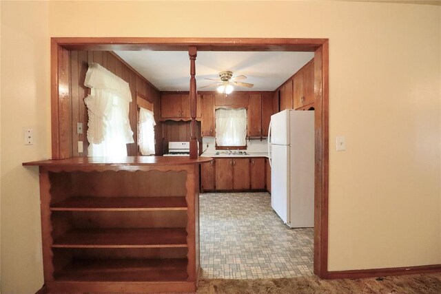 kitchen featuring baseboards, brown cabinetry, a ceiling fan, freestanding refrigerator, and a sink