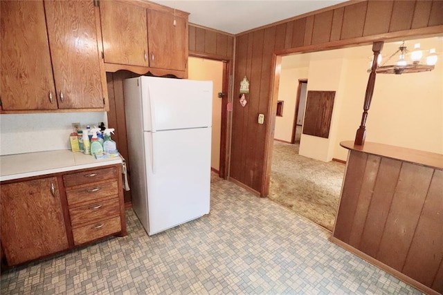 kitchen featuring light countertops, brown cabinetry, freestanding refrigerator, light carpet, and wood walls