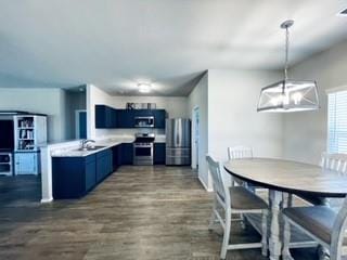 kitchen with light countertops, appliances with stainless steel finishes, hanging light fixtures, blue cabinetry, and dark wood finished floors