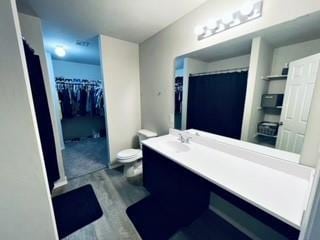 full bath featuring curtained shower, vanity, toilet, and a walk in closet