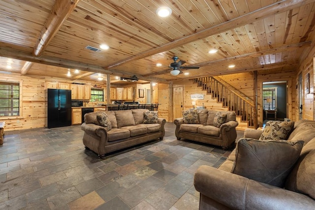 living room with beam ceiling, stone tile floors, stairway, wood ceiling, and wood walls