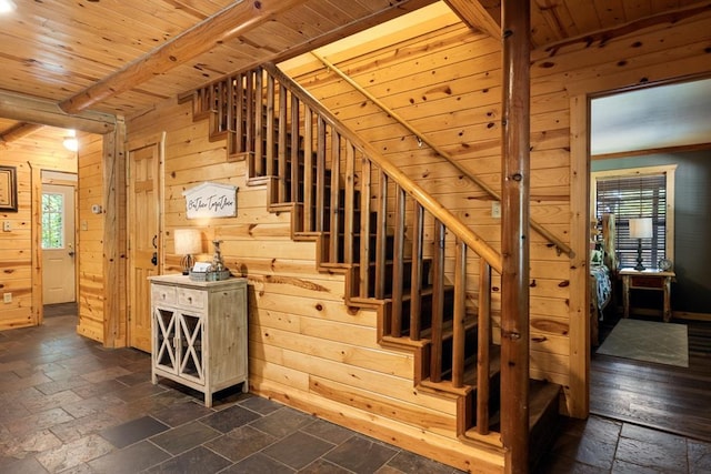 staircase with wooden ceiling, wood walls, stone tile floors, and beam ceiling