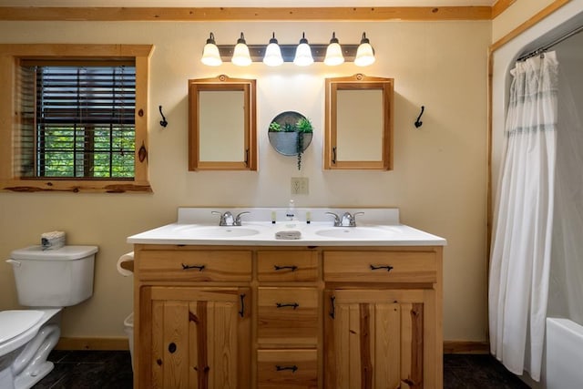 full bathroom featuring toilet, double vanity, baseboards, and a sink