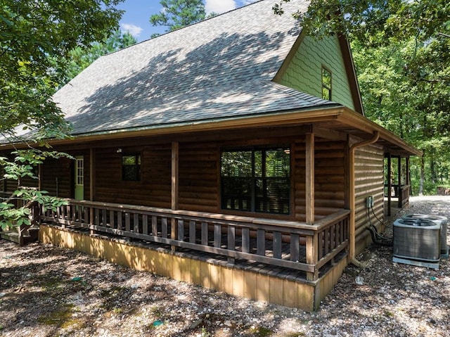 view of side of property featuring covered porch, central AC, a shingled roof, and log veneer siding