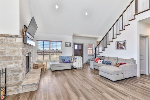 living room with a towering ceiling, stairway, wood finished floors, a stone fireplace, and recessed lighting